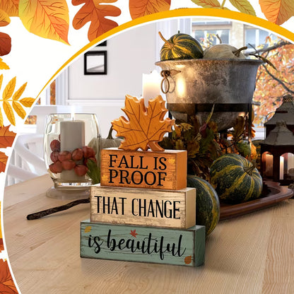 Wooden 'Fall Is Proof That Change Is Beautiful' block sign with maple leaf on an autumn table with pumpkins
